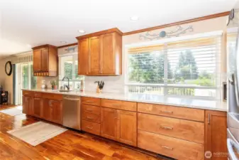 This wide-angle view showcases the kitchen’s impressive counter space, stretching nearly the full length of the room. Large windows above the sink bring in daylight and connect the home to the outdoor scenery. Rows of cabinets and drawers offer storage galore, while sleek stainless steel appliances ensure the kitchen is ready for modern living. It’s both efficient and elegant, built for convenience without sacrificing charm.
