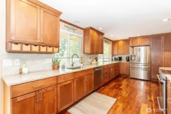 This view highlights the kitchen’s stainless steel refrigerator, dishwasher, and range, blending seamlessly with custom cabinetry. The expansive counters provide ample prep space, while the layout keeps everything within easy reach. With multiple windows and warm wood finishes, the kitchen feels open, bright, and practical. Whether you’re cooking for one or hosting many, this kitchen is designed to make life easier while looking great.