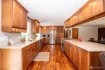 This angle captures the full symmetry of the kitchen. Dual rows of cabinets and counters create a balanced, functional workspace. The overhead cabinetry adds storage without compromising openness, while recessed lighting ensures a bright, welcoming environment day or night. The kitchen’s design blends modern updates with timeless craftsmanship, making it both efficient and stylish—a true centerpiece of the home.