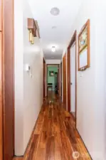 The hallway ties the home together, featuring beautiful wood flooring that flows throughout the main living spaces. Warm tones create an inviting atmosphere, while multiple doors open to bedrooms, bathrooms, and storage areas. It’s a functional hub that highlights the home’s simple, practical design. The updated floors provide a polished look and add character to this well-kept home.