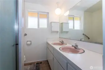 This bathroom showcases double sinks with vintage charm and functionality. Large mirrors and built-in cabinetry provide both space and convenience. The layout is simple yet efficient, with a shower and window for light and ventilation. The retro details, like the pink basins, give a nostalgic feel while offering an opportunity for creative updates. It’s a practical bathroom that’s move-in ready but also primed for modernization.