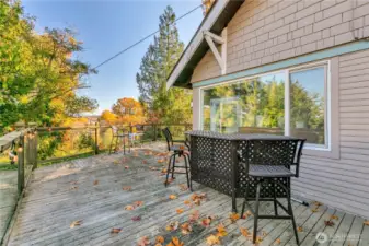 Expansive wraparound deck with clear panel railing along the north & east sides, leading to the front entrance.