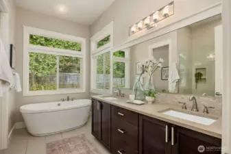 Light-filled primary bath with dual vanities, soaking tub, and serene garden views.