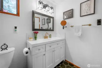 Main Level Bathroom – Updated vanity with sleek lighting, gold hardware, and stylish black hex tile.