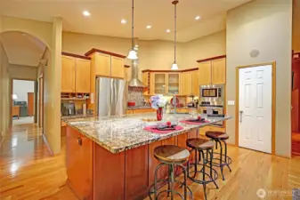 Chef’s kitchen with stainless steel appliances, granite counters, honey oak hardwood floors, pantry.   See sconce lit hallway to guest wing, laundry and garage. In wall speakers provide whole house sound system.