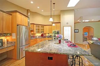 Kitchen view showing work desk, French door refrigerator, granite island with dishwasher, wall ovens and pantry.  Archway leads to home office.