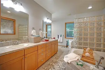 Primary spa-like bath boasts heated tile floors, his and hers vanities with generous cabinetry, deep soaking tub and large glass block enclosed shower with two shower heads.