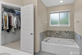 The primary bathroom is a true retreat, with a ceramic-tiled floor, soaking tub, dual sinks, and a spacious walk-in closet. Sunlight gently brightens the room through privacy-friendly glass.