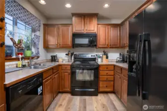 Kitchen with laminate flooring. Black appliances compliment the wood cabinets nicely.