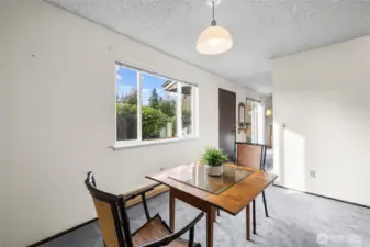 Dining area with a large window overlooking the entry and surrounding greenery.