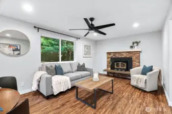 ?? Cozy Living Room with Timeless Charm!  Relax and unwind in this inviting living space featuring warm wood-style flooring, fresh neutral paint, and a large window that fills the room with natural light. The focal point is the classic brick fireplace with a wood-burning insert—perfect for chilly evenings. Modern updates like recessed lighting and a sleek ceiling fan blend effortlessly with the room’s cozy, welcoming feel.