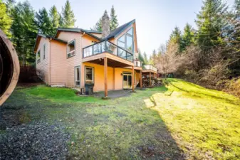 Exterior rear of home. Doors out from the basement into the lawn. Main floor deck overlooks the greenery outside.