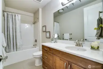 Conveniently located just off the family room, this full bath serves both shared and private spaces—featuring quartz counters, sleek tile flooring, and timeless design.