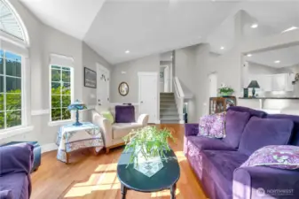This living area features soaring ceilings, large windows, and warm hardwood floors. The open layout flows beautifully toward the kitchen and staircase, creating an inviting first impression.