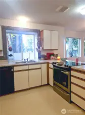 A closer look at the kitchen showcases its generous counter space, classic cabinet layout, and a bright corner window that brings in natural light throughout the day. This functional design offers plenty of room for meal prep and everyday living, all while staying connected to the rest of the home.