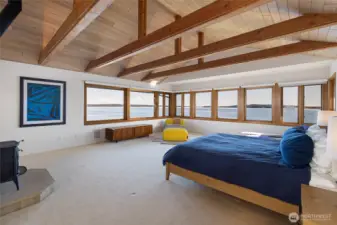 Expansive primary suite with vaulted ceilings, exposed beams, and panoramic water views, offering a peaceful retreat immersed in the surrounding landscape.