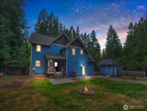 Twilight shot of the back yard. Back elevated porch leads to the main kitchen. Lit door on the right leads to the secondary small kitchen.