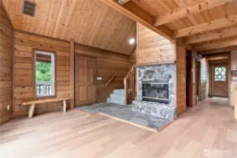 View to the front entryway and the back entry as well. The back door is also solid wood. The custom wood fireplace is central to this home, stone flooring and fireplace.