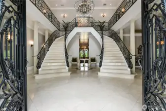 Grand imported glass-and-iron doors that open into a breathtaking entryway. Inside, dual curved, Italian marble staircases with custom iron scrollwork rise beneath curated Restoration Hardware lighting.