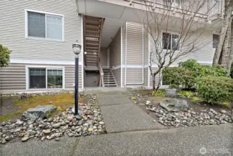 Well-maintained multi-story building with a concrete walkway, mature landscaping, and easy stair access to upper units.