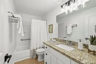 Updated full bath with granite vanity, white cabinetry, modern globe light fixture, and tub/shower combo.