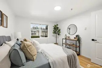 Bright bedroom corner with large windows, hardwood floors, and open views of the surrounding greenery.