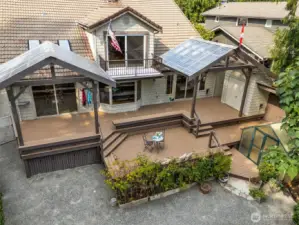 Pictured: Large tiered deck, with portions covered, upper level balcony, shed & green house.