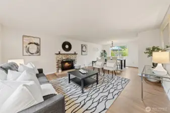 The inviting living room showcases a wood-burning fireplace with a chic mantel, rich laminate floors, and a flow to the kitchen, dining area, and entryway. Its open layout creates a warm and connected   space for both relaxing and entertaining.