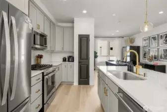 Quartz island with gold fixtures, and pendent lighting, opens to living and dining