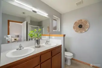 Double vanity, toilet and walk-in-shower in background.