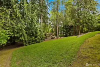 The property is surrounded by a lush green lawn and majestic evergreen trees, offering beauty and privacy in every direction.