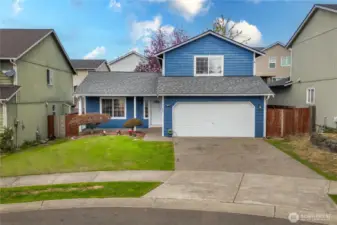 Classic curb appeal with fresh blue siding, a covered front porch, and a two-car garage. Manicured landscaping adds a welcoming touch.