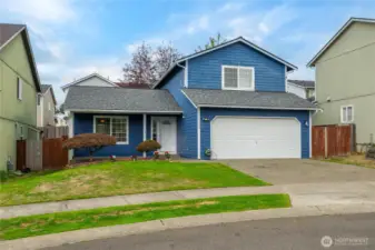 A slightly angled view highlights the wide driveway and front yard, offering extra parking in addition to the garage.