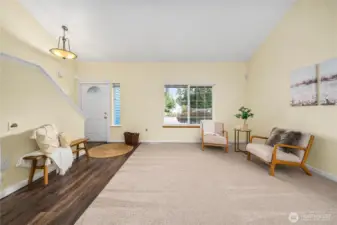 The entry opens into a bright living space with vaulted ceilings and fresh, neutral paint. A large picture window fills the room with natural light while showcasing views of the front yard.