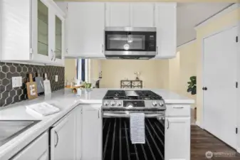 This angle highlights the gas range with overhead microwave and abundant counter space on either side. Crisp cabinetry and updated finishes create a clean, inviting cooking environment.