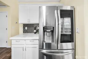 A stainless steel French-door refrigerator anchors this side of the kitchen, set against generous counter space and cabinet storage. The modern tile backsplash ties the design together.