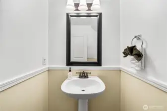 A closer look at the half bath highlights the pedestal sink and framed mirror under a stylish light fixture. Clean finishes and neutral tones create a fresh, functional space.