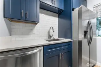Updated kitchen featuring quartz countertops, custom cabinets, stainless steel appliances, and tiled backsplash.