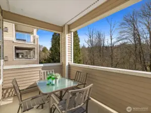 Covered deck with seating area overlooking private wooded greenbelt, providing outdoor space with territorial views and year-round usability.