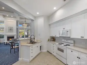 Community kitchen with cabinetry, sink, range, microwave, and open connection to clubhouse seating areas. Shared amenity space for gatherings and events.