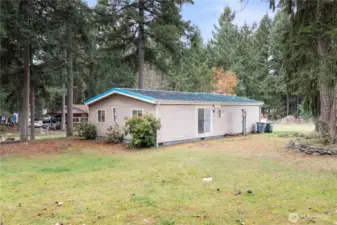 A view of the side and rear of the home, showing the level yard and the quiet forest backdrop. This angle highlights the sliding door leading to the main living area and gives buyers a sense of the home’s natural surroundings and the usable outdoor space.