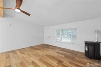 An unstaged view of the living room, showing its open layout, wide-plank flooring, and large front window that brings in natural light. The wood-burning stove sits at the corner of the room, ready to warm the space. This photo gives buyers a clear look at the room’s size and potential.