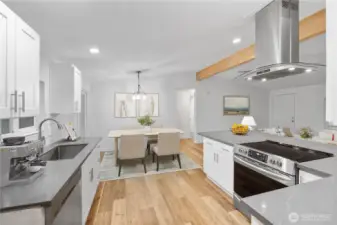 A bright, refreshed kitchen and dining area with white cabinetry, quartz-style counters, and warm wood flooring. The open layout flows easily into the dining space, which is styled to show how much room there is for everyday meals or entertaining. Clean lines, modern lighting, and natural light create a welcoming central hub of the home.