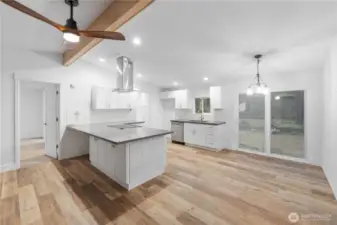 An open view of the kitchen and dining space, showing how the layout flows naturally toward the sliding doors and outdoor area. The island offers additional seating and workspace, while the warm wood flooring ties the entire great-room area together. This angle helps buyers visualize the home’s flexible everyday living and entertaining potential.