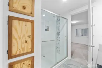 The master bath features a fully tiled walk-in shower with a glass door, accent tile column, and a built-in niche for essentials. Clean white finishes keep the room bright, and the layout offers a straightforward flow into the adjoining bedroom.