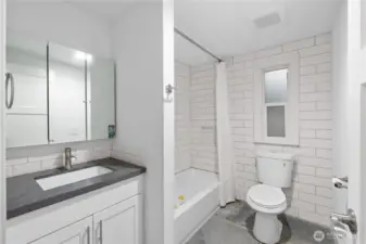 Bright and refreshed hall bath featuring a modern vanity with quartz counters, subway tile backsplash, and a full tub/shower surrounded by clean, oversized white tile. The frosted window brings in natural light while maintaining privacy, and the neutral finishes make this space move-in ready for guests or everyday use.