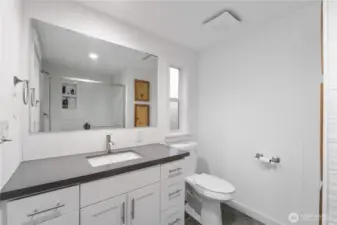 A clean and modern primary bath featuring a wide quartz-topped vanity, full-width mirror, and updated fixtures. The large walk-in shower with sliding glass doors and decorative tile accents adds a polished feel. Bright lighting and simple white paneling keep the space fresh and calming.