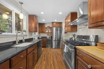 The updated kitchen shines with cherry cabinets, quartz and butcher block counters, and a dual fuel, professional range from Kenmore. On the far wall, a brand new beverage fridge sits next to a Bosch refrigerator that was purchased in 2024. Above the range, a brand new hood vent hovers over a handy pot filler.