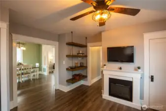 The family / flex room is off the dining room, with an electric fireplace, ceiling fan and custom shelving.