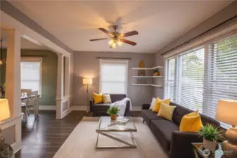The living room is light and bright with tall ceilings, corner shelving and ceiling fan, with beautiful easy care updated LVP flooring and white trim throughout the home .